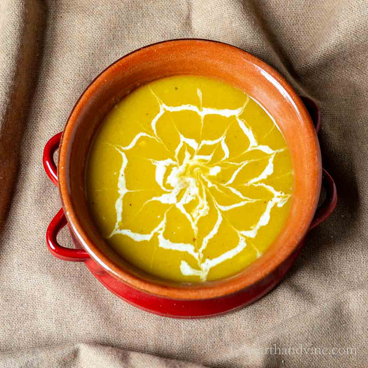 Bowl of delicata squash soup with a spider web design on top made with cream.