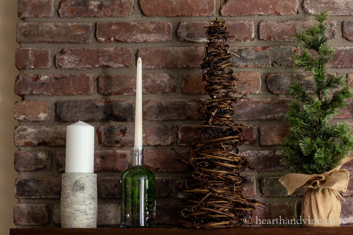 Mantel with a candles a faux pine tree and a grapevine tree.