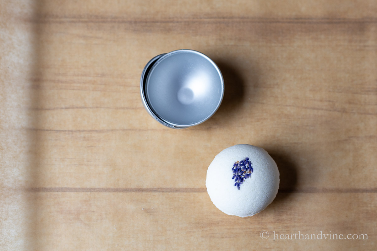 One lavender flower bath bomb next the metal mold it came out of.