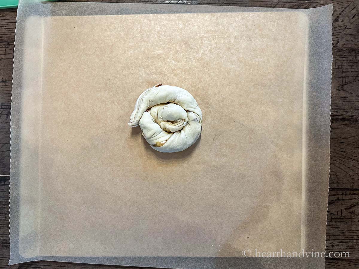 One of the cut rolled pastry placed on parchment on a baking sheet beginning in a tight spiral shape.