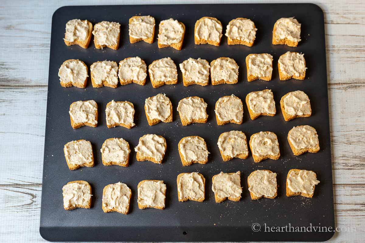 Mini toasts with cheesy spread on a baking sheet.