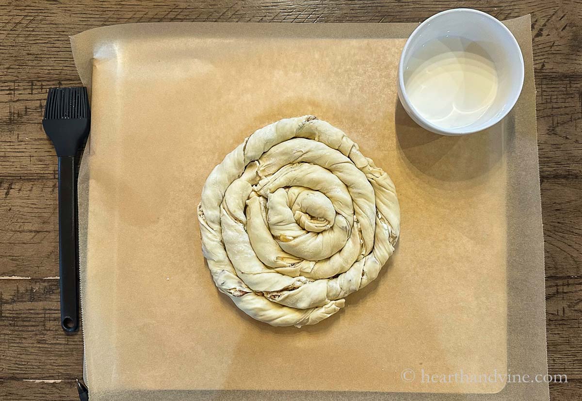 The full spiral puff pastry with a pastry brush and a bowl of half and half.