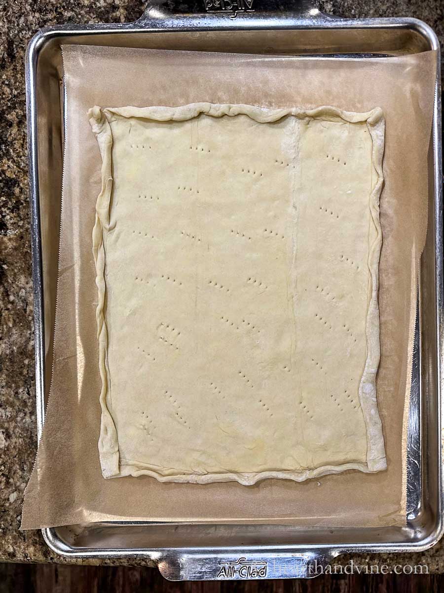 Sheet of puff pastry with folded edges and fork marks on parchment lined baking sheet.