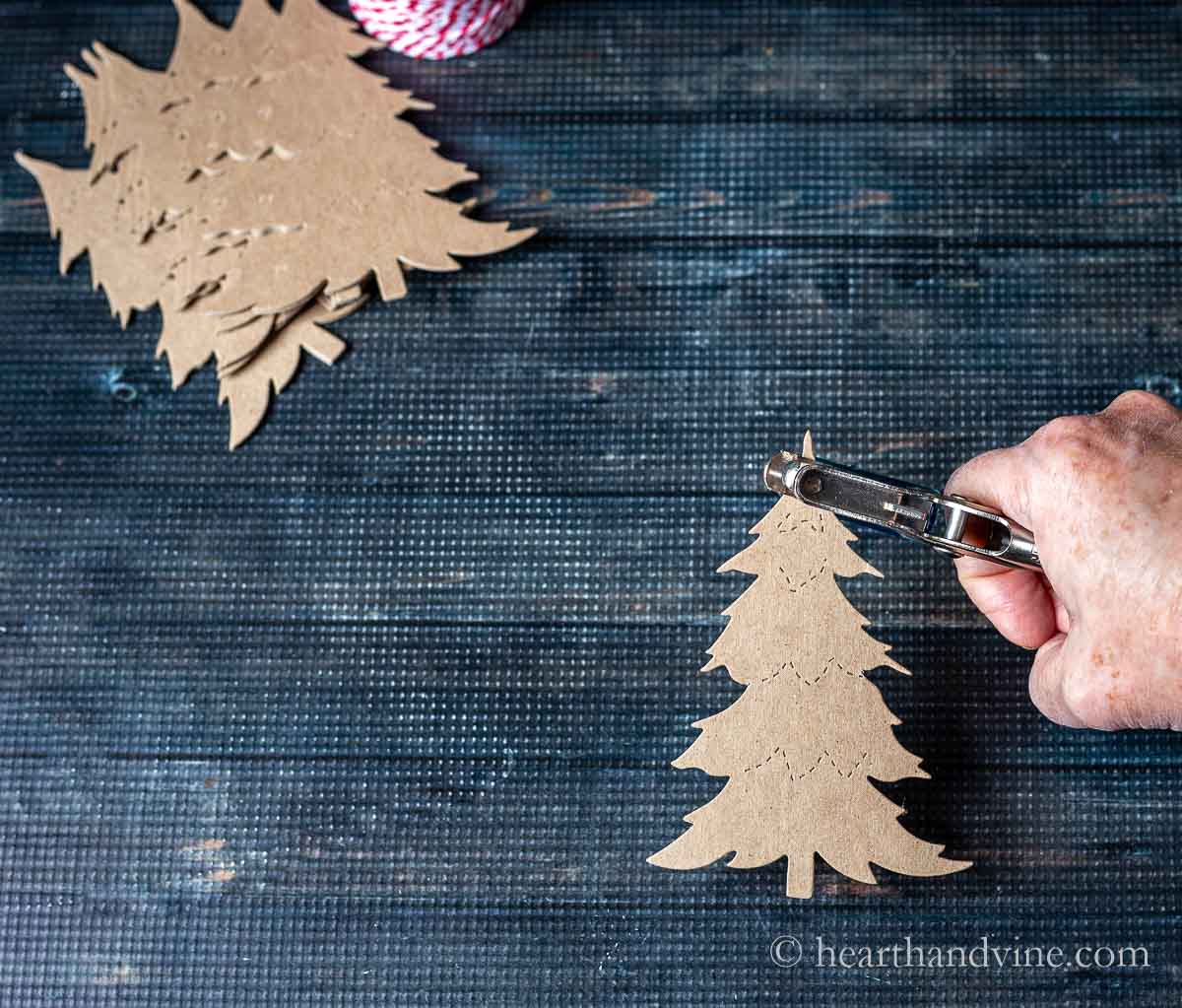 A hand punching a small hole at the top  of a chipboard Christmas tree shape.