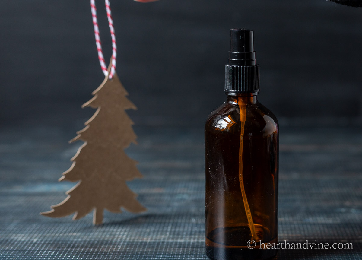 A chip board shipped evergreen tree with a red and white twine hanger next to an amber spray bottle.