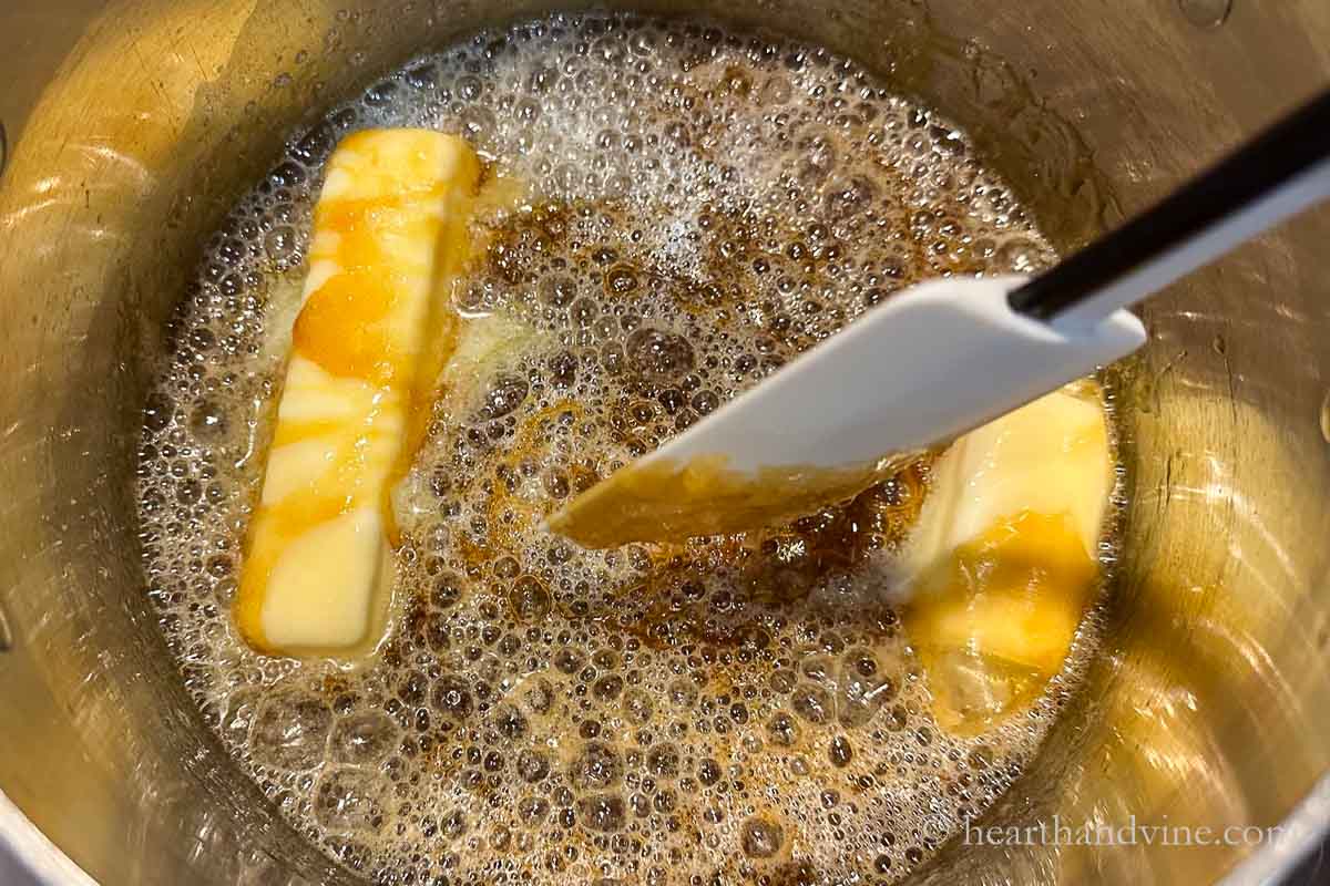 Butter adding to melted sugar in a pot on the stove with a spatula stirring.