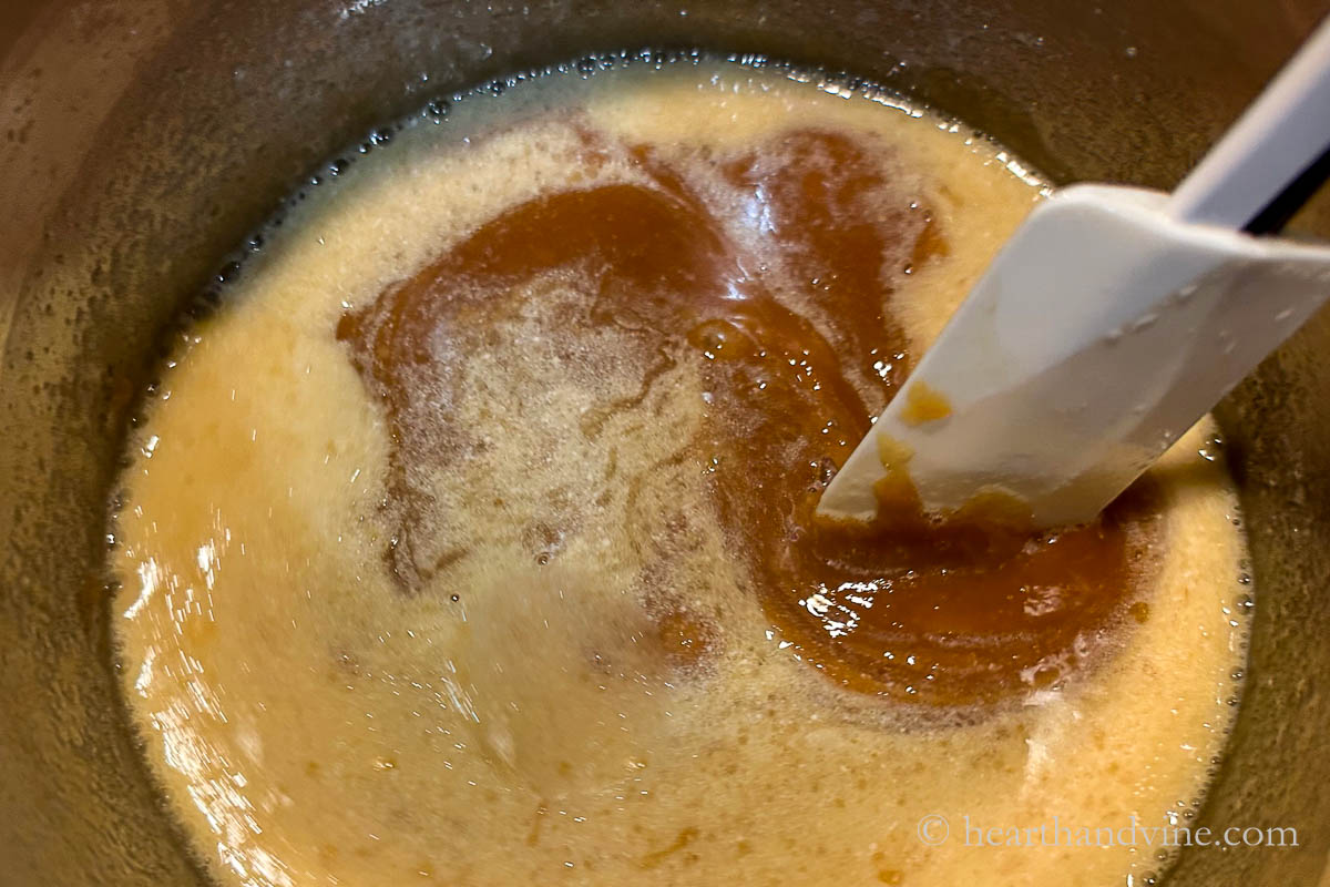 Cream added to the sugar and butter mixture in a pot on the stove with a spatula mixing them all together.