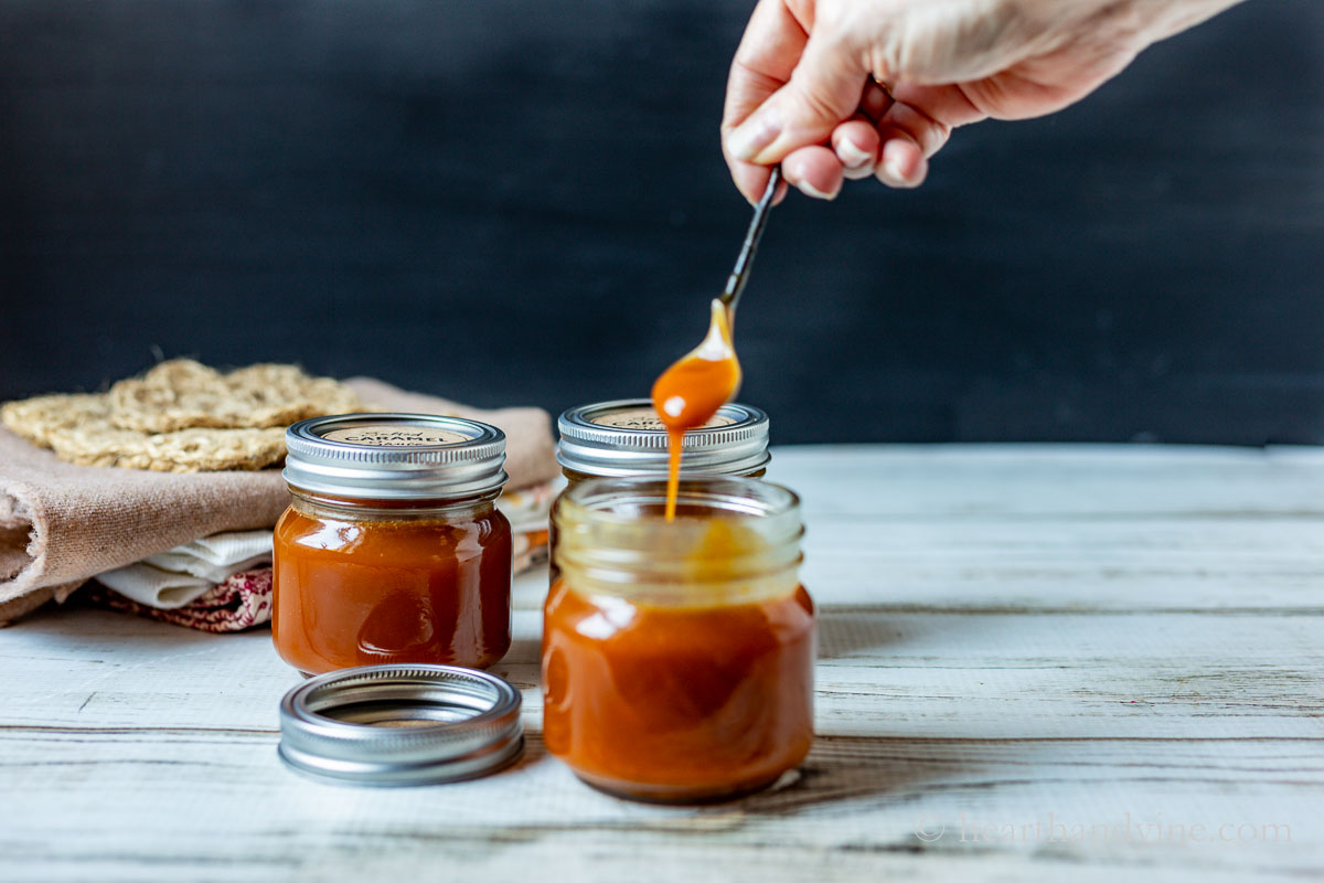 A couple of jars of salted caramel sauce. One is open with a small spoon lifting up some of the sauce.