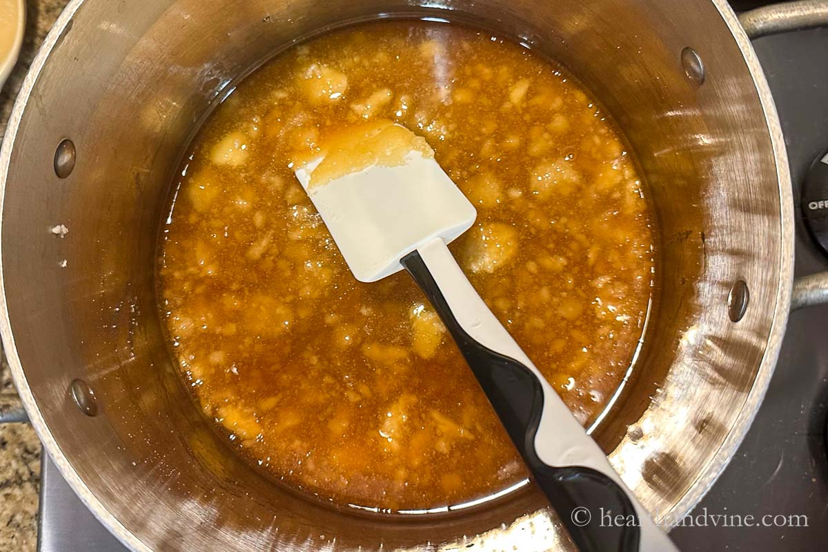Sugar starting to melt in a pot on the stove with a rubber spatula.