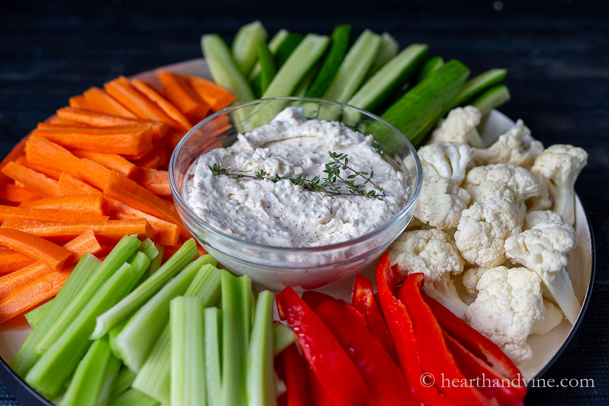 A tray of cut up vegetables with a bowl of dip in the middle.