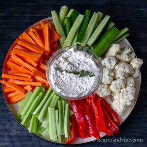 Cream cheese vegetable dip surrounded by cut up carrots, celery, cucumbers, red peppers and cauliflower florets.