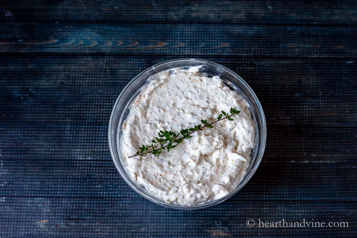 A bowl of cream cheese veggie dip with  a sprig of fresh thyme on top.