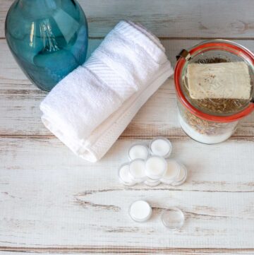 Small containers of cuticle cream with a couple of white tiles, a jar of bath salts and a blue vase.