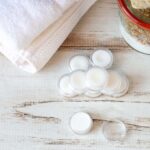 Small clear containers of cuticle cream next to white rolled towels.