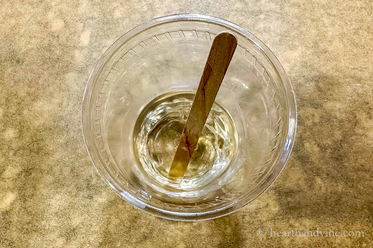 Cup with melted beeswax in a oil with a wooden stick.