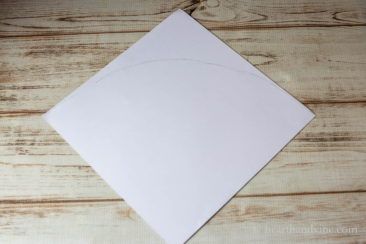 A square piece of paper with a line drawn from one point to the other making an arch.