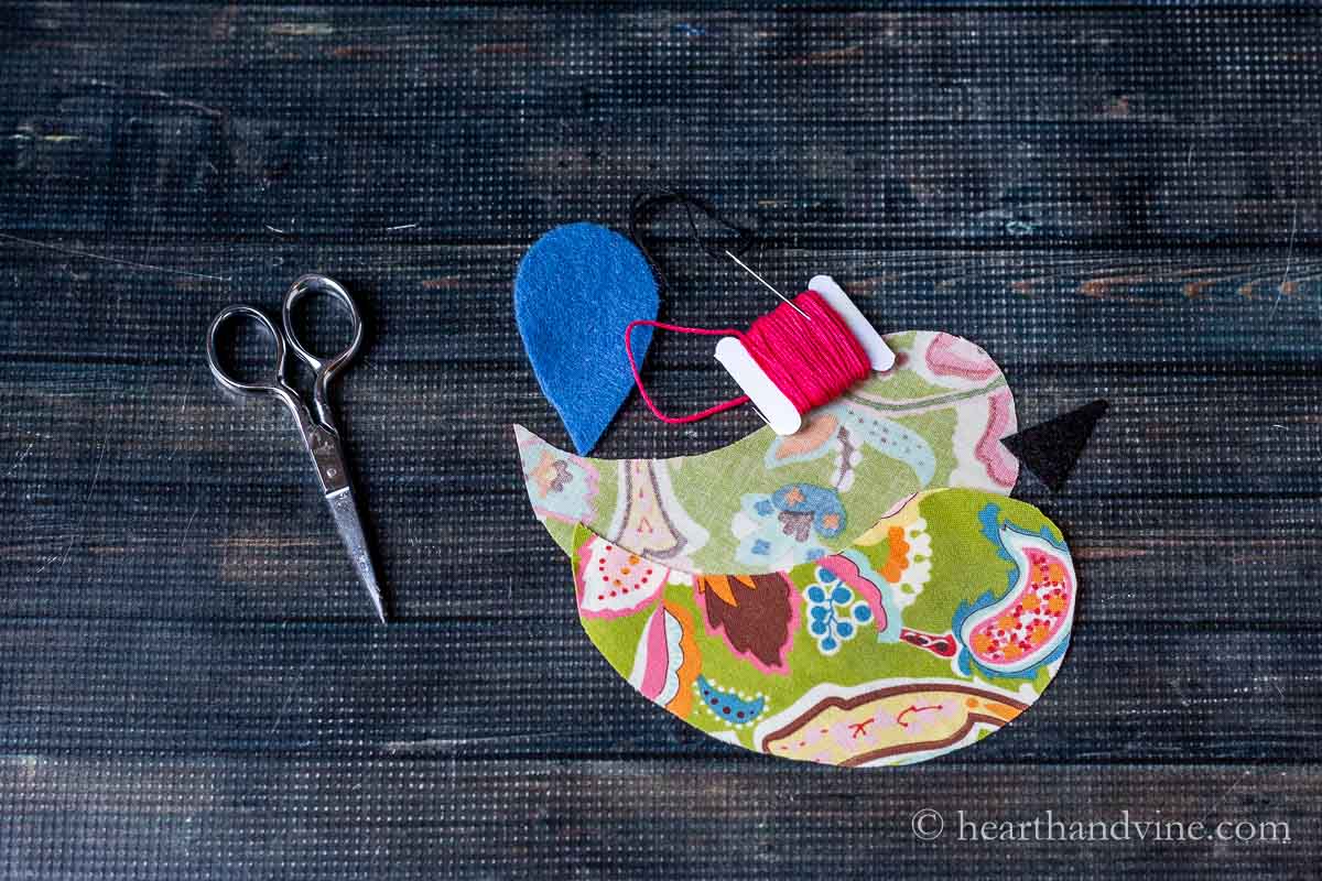 Cut out bird shapes in fabric, a pair of scissors, pink embroidery thread, and a needle.