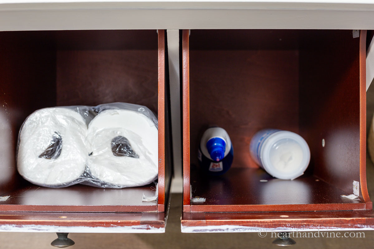 Inside of cabinet bins with toilet paper on one side and cleaning products on the other.