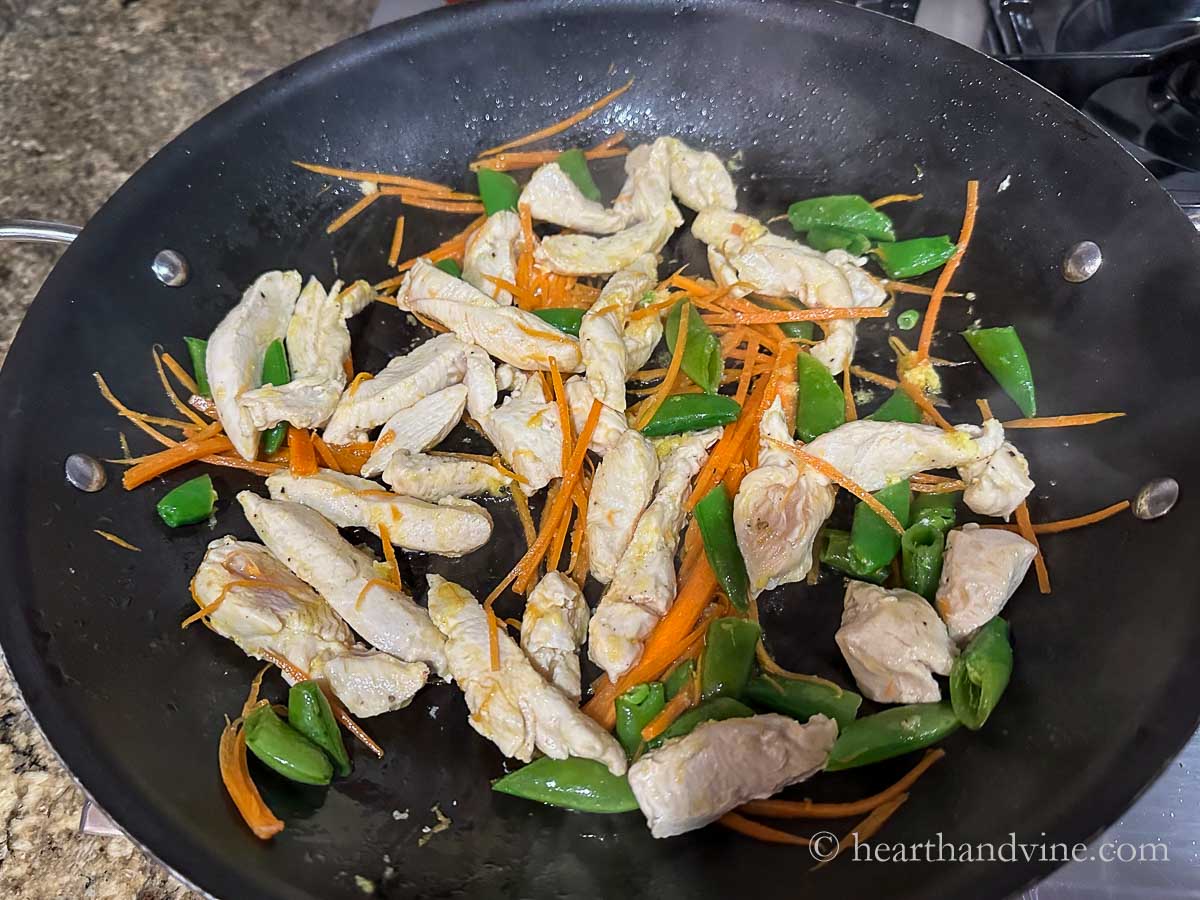 Chicken strips, carrot sticks and snap peas sauteing in a pan.