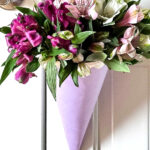 A bouquet of flowers hanging on a door in a pretty lavender paper cone with pink ribbon edging.