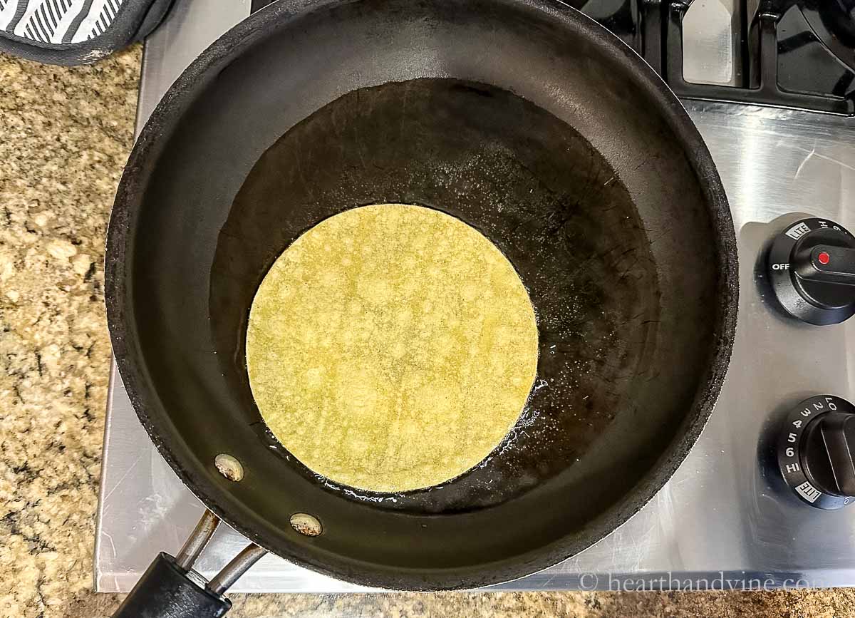 Frying a corn tortilla in vegetable oil on the stove.