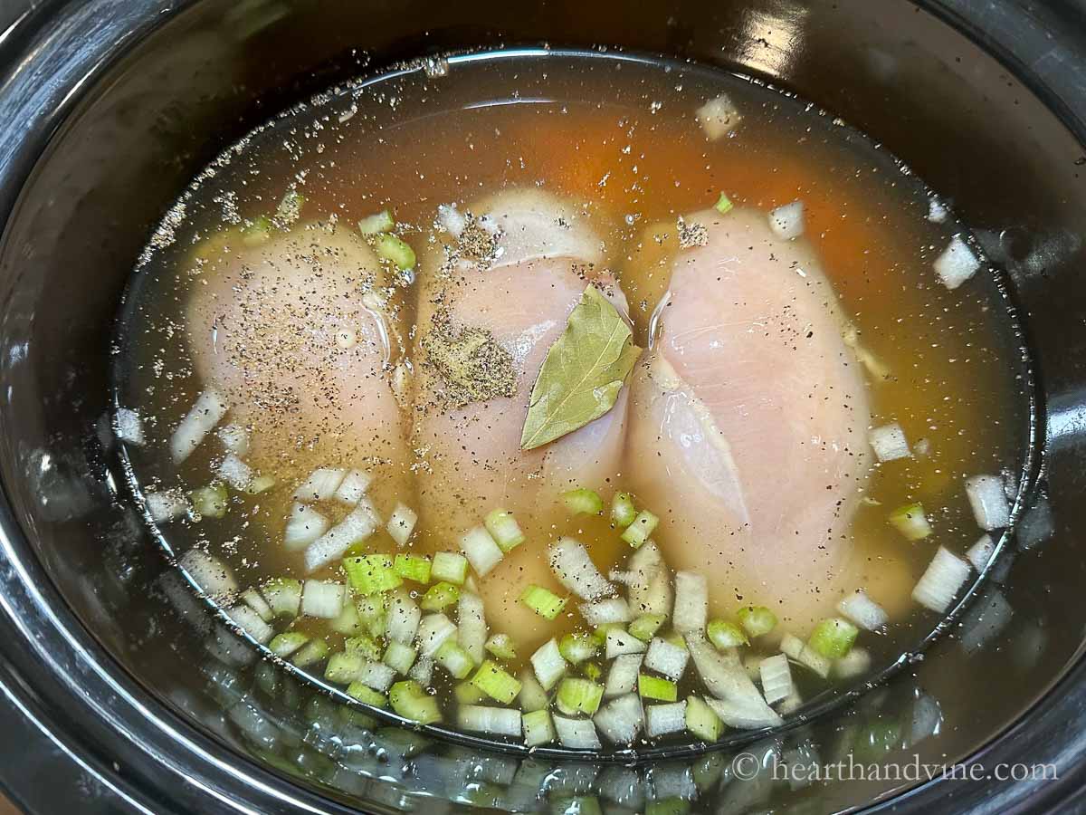 Slow cooker with vegetables, seasoning three chicken breast and broth.