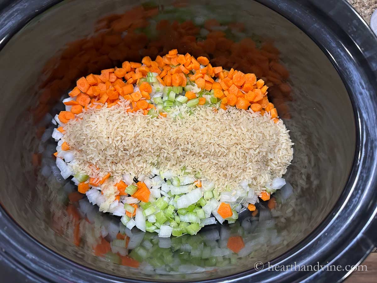 Cut up carrots, onions and celery and long grain uncooked rice in a slow cooker.