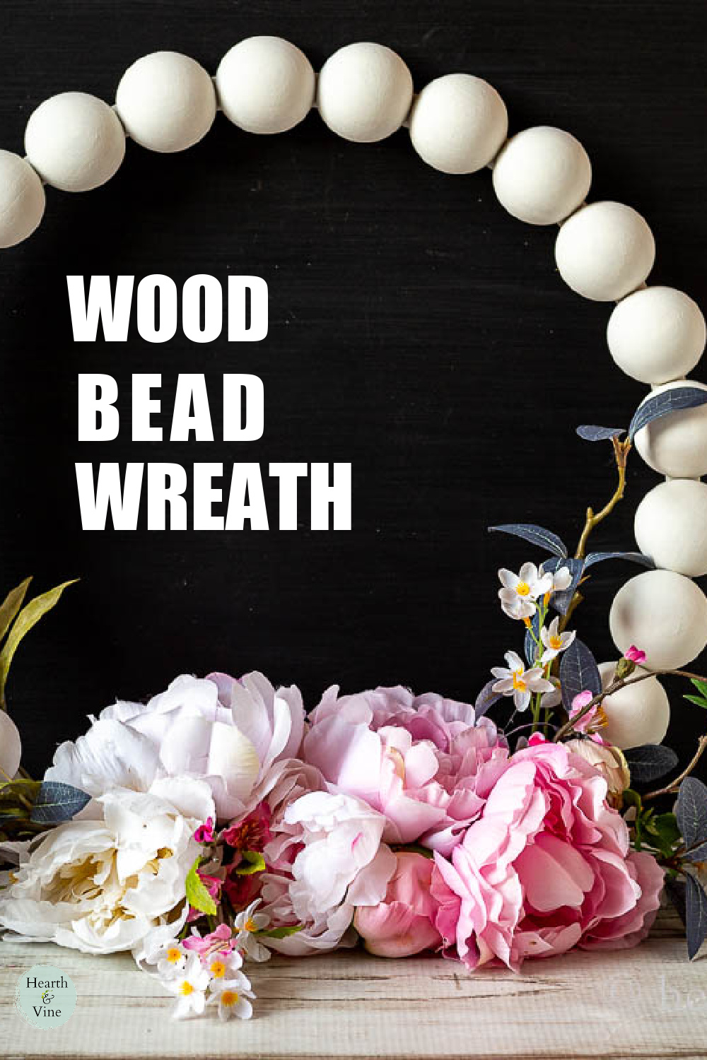 Partial view of a white wooden bead wreath with artificial peonies, blossoms and leaves.