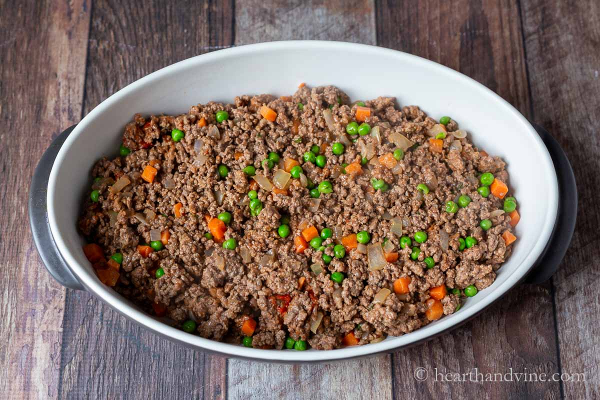 Ground beef mixture with carrots and peas layered into the bottom of a baking pan.
