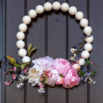 Off white wooden bead wreath with spring flowers hanging on a front door.