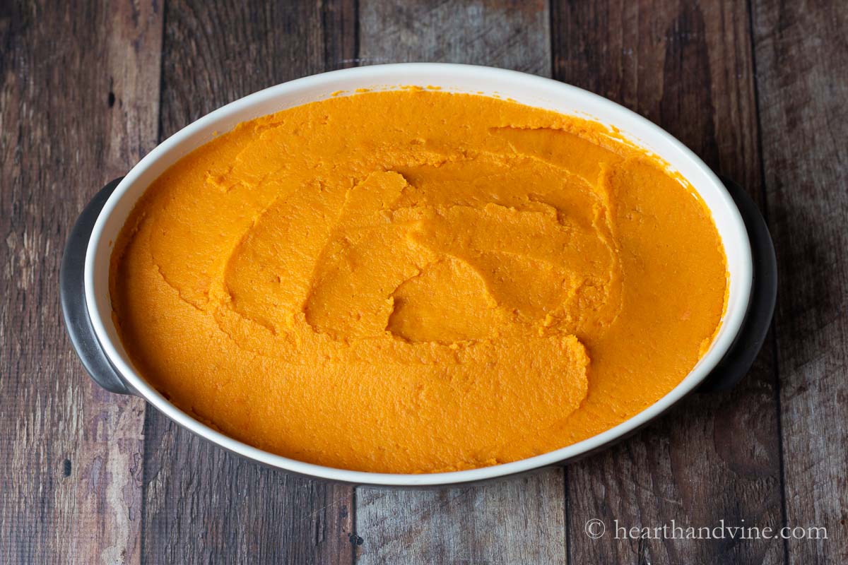Mashed sweet potatoes spread over beef mixture in a baking pan.