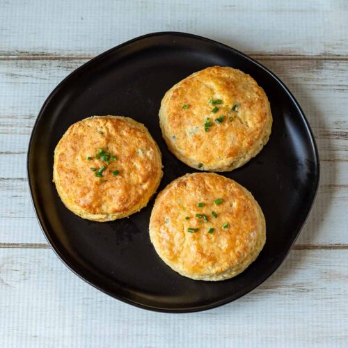 Three cheddar and chive biscuits on a plate.