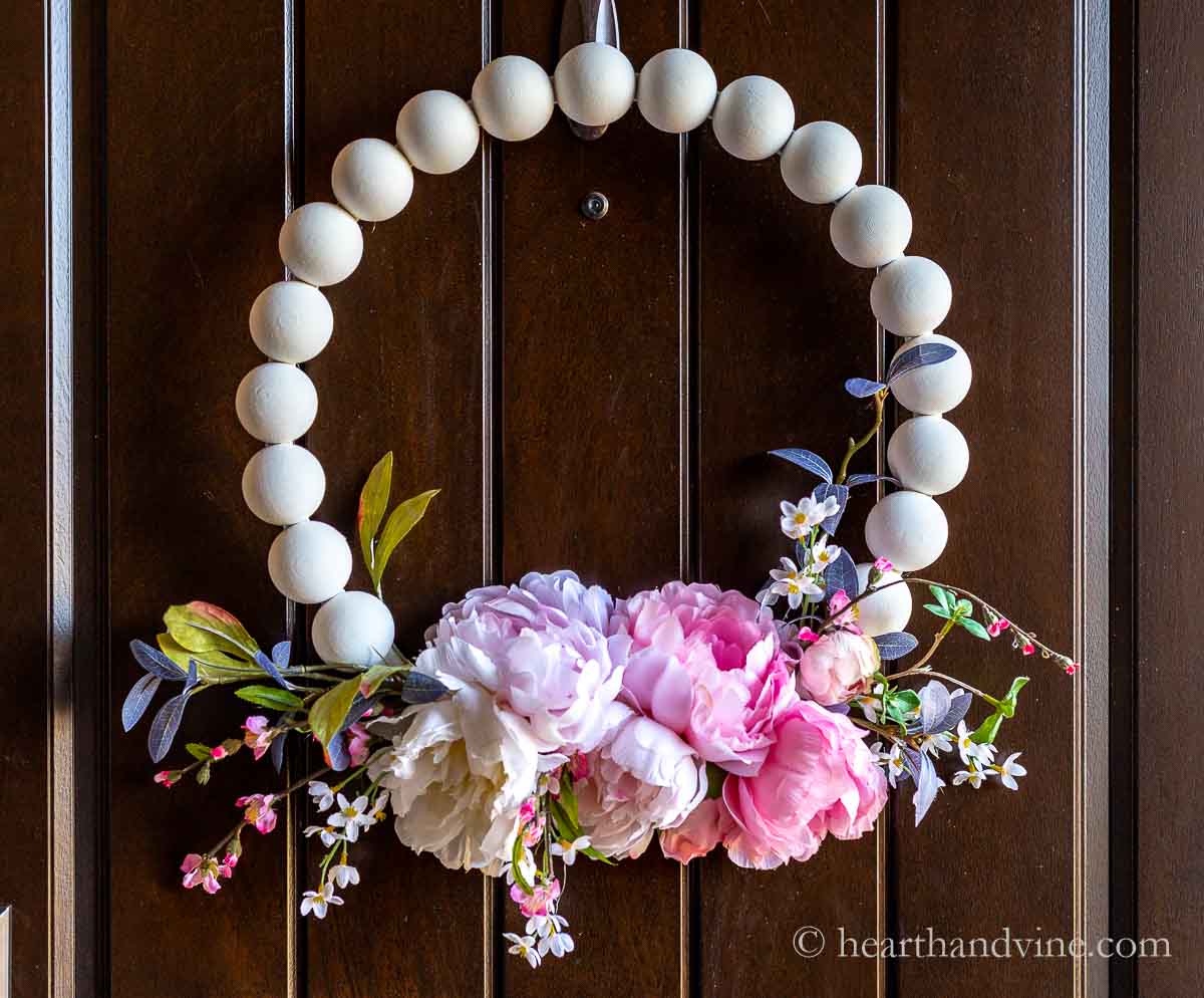 White wooden bead wreath with faux peonies and spring blooms.