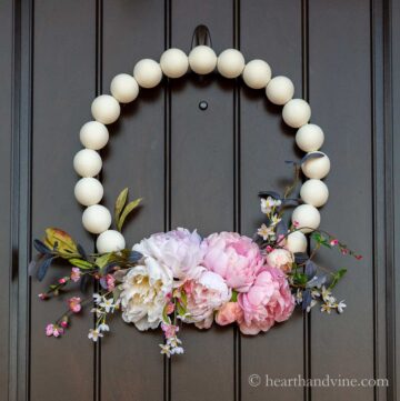 Wooden bead wreath with flowers on a dark front door.