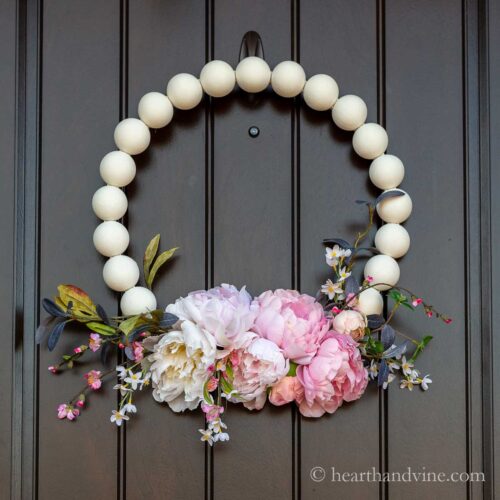 Wooden bead wreath with flowers on a dark front door.