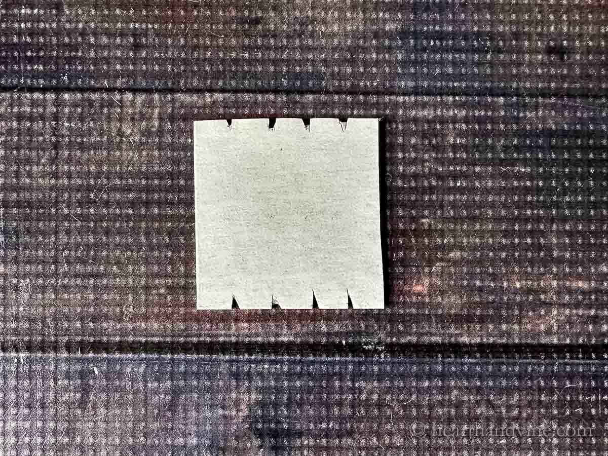 A square piece of cardboard with notches cut into the top and bottom.