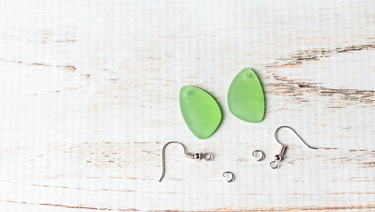 Two sea glass pendants with holes and two jump rings and two earring hoops.