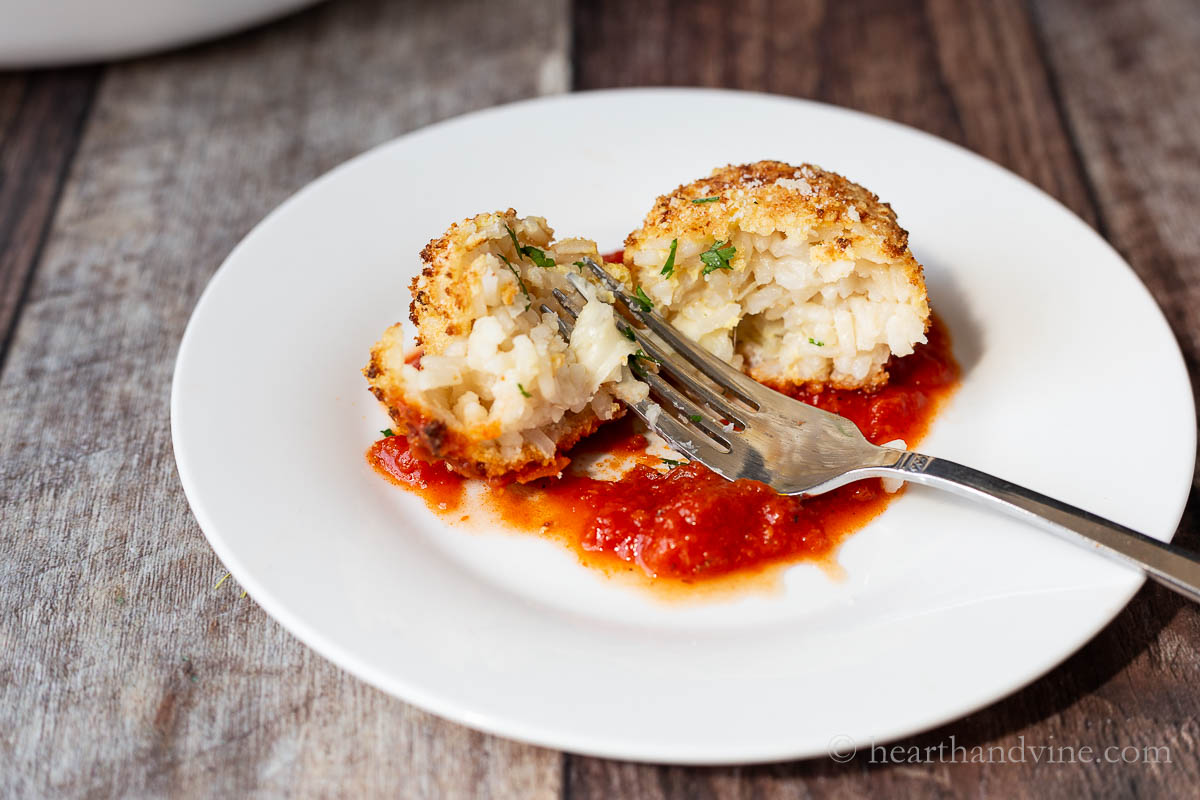 A plate with marinara sauce and one arancini cut open with a fork.