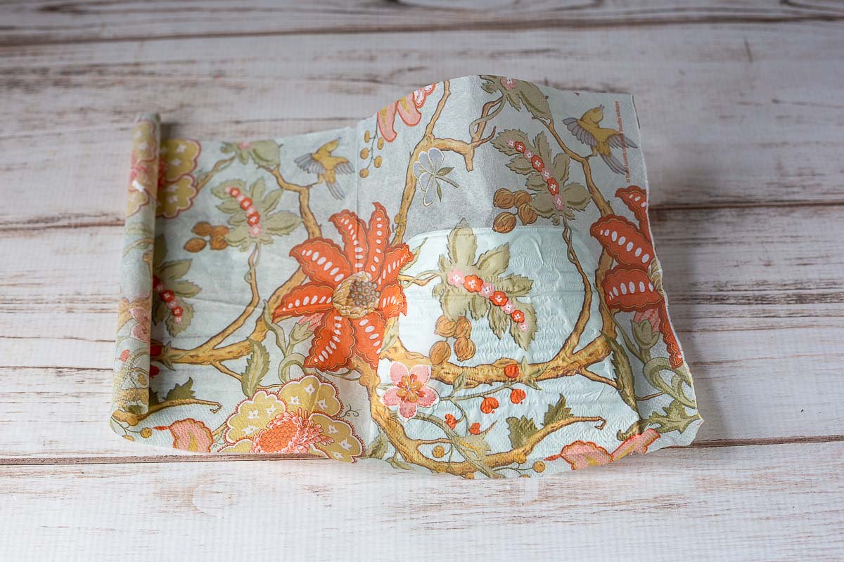 A pretty peach and blue floral printed paper napkin set over one side of the can that has been coated with Mod Podge.