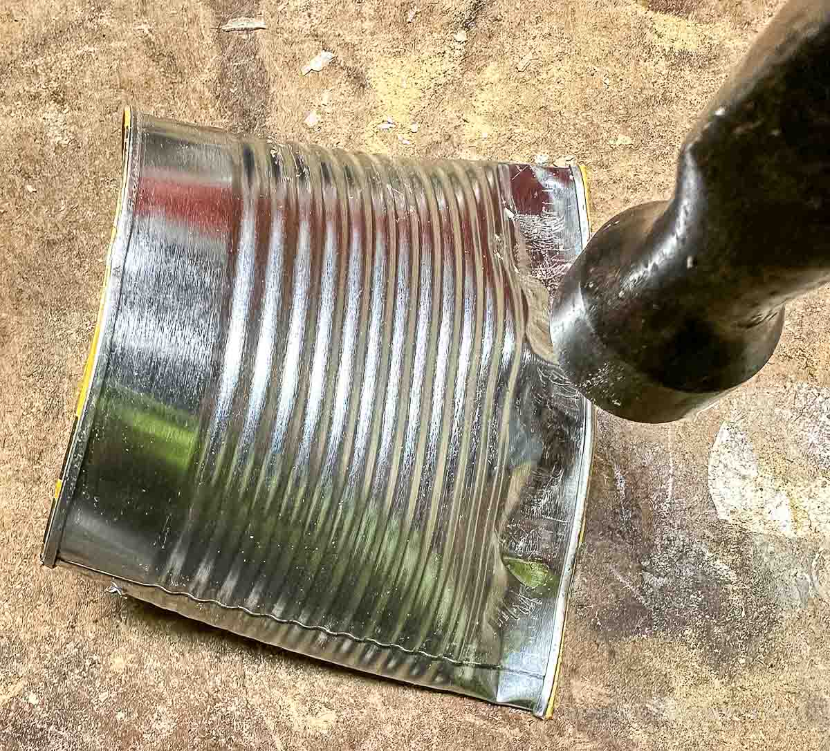 A hammer crushing the bottom of a tin can to crimp closed.