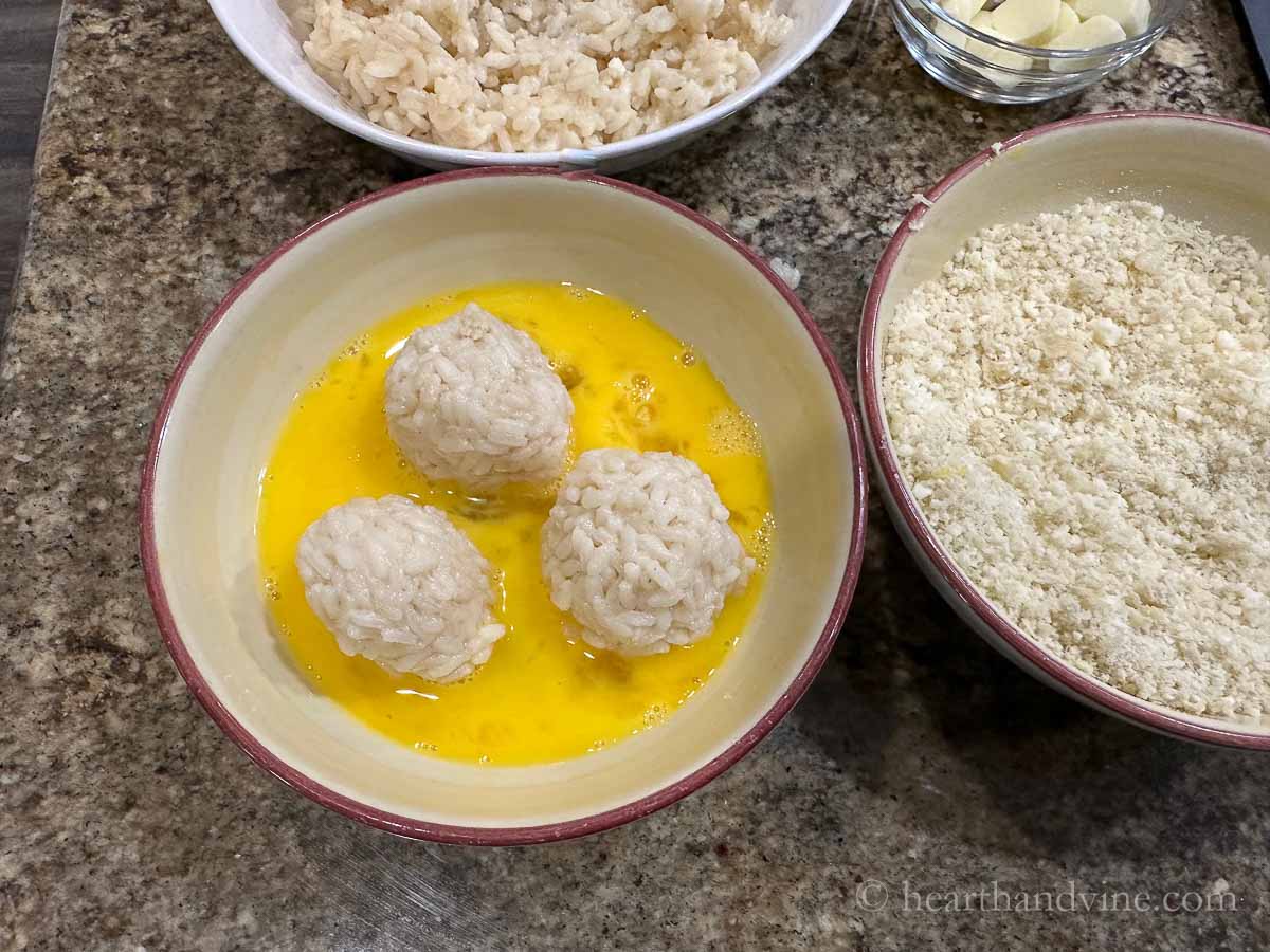 Three risotto balls in a bowl of beaten eggs.