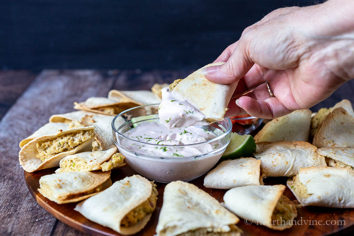 A hand dipping a mini chicken quesadilla into crema.