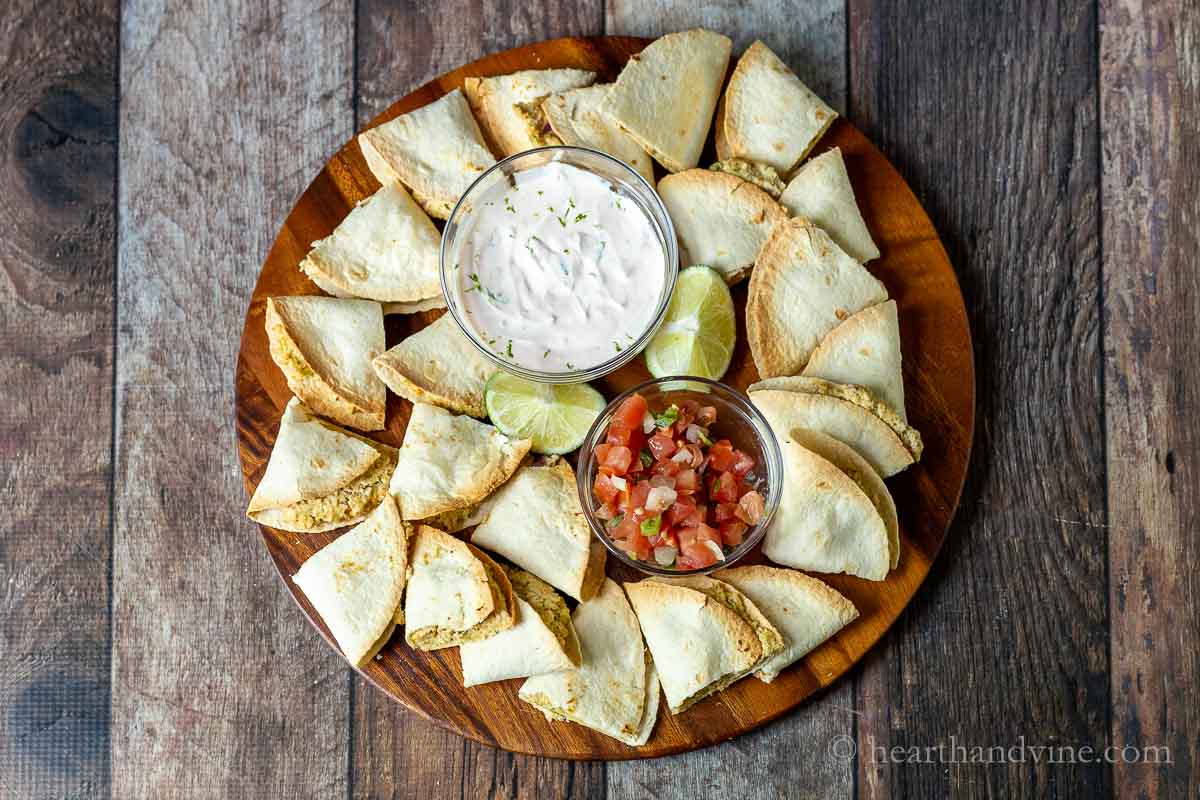 Mini chicken quesadillas on a serving platter with lime wedges, a bowl of crema and a bowl of pico de gallo.