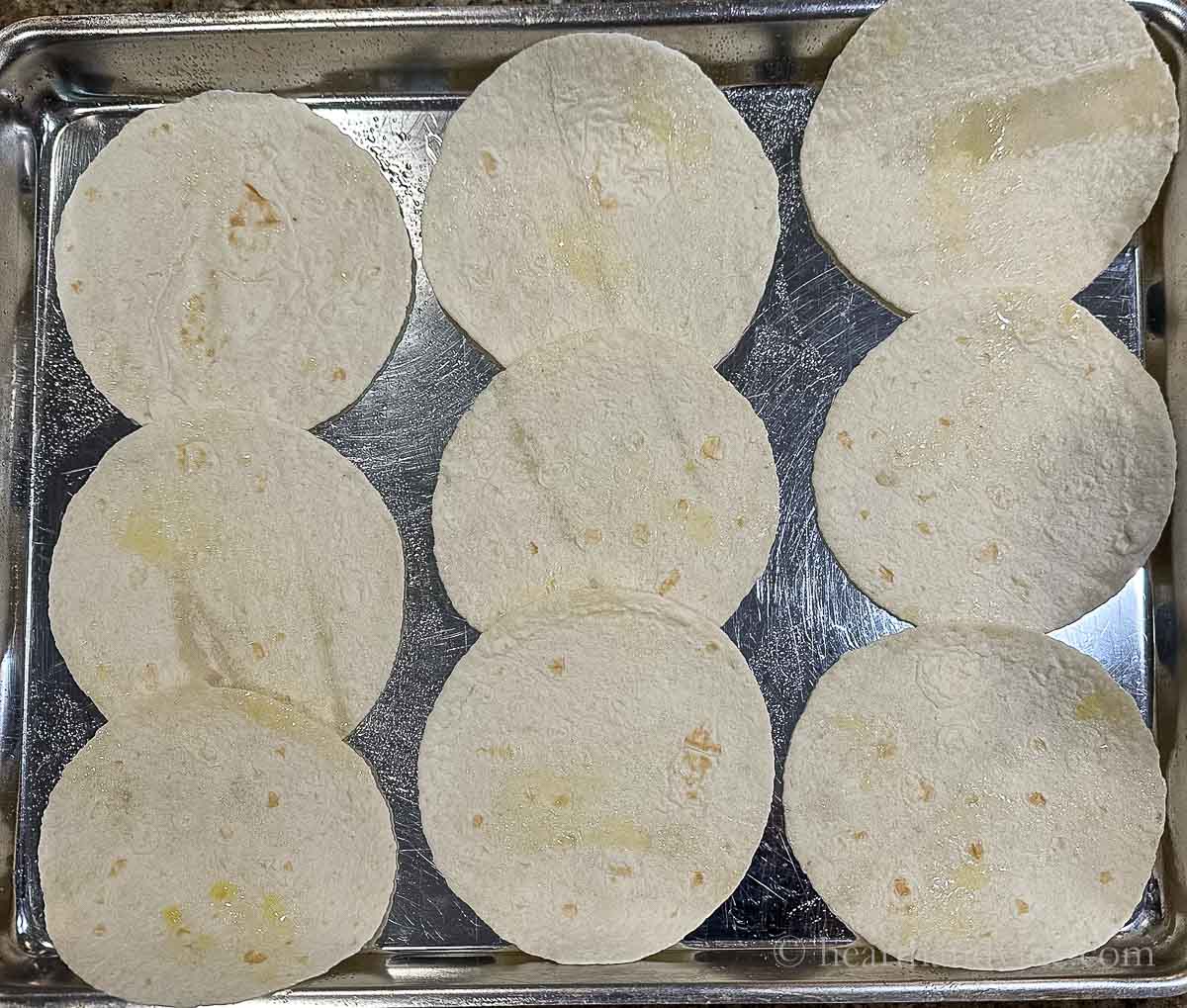 Small 5-inch tortillas with olive oil spray on a baking sheet.