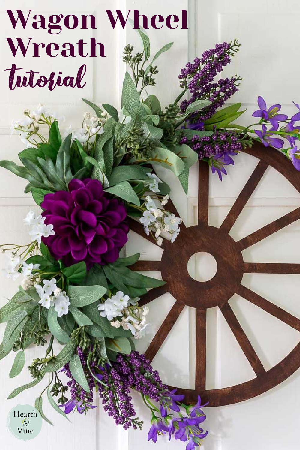 Brown wagon wheel wreath with purple, and white flowers and greenery.