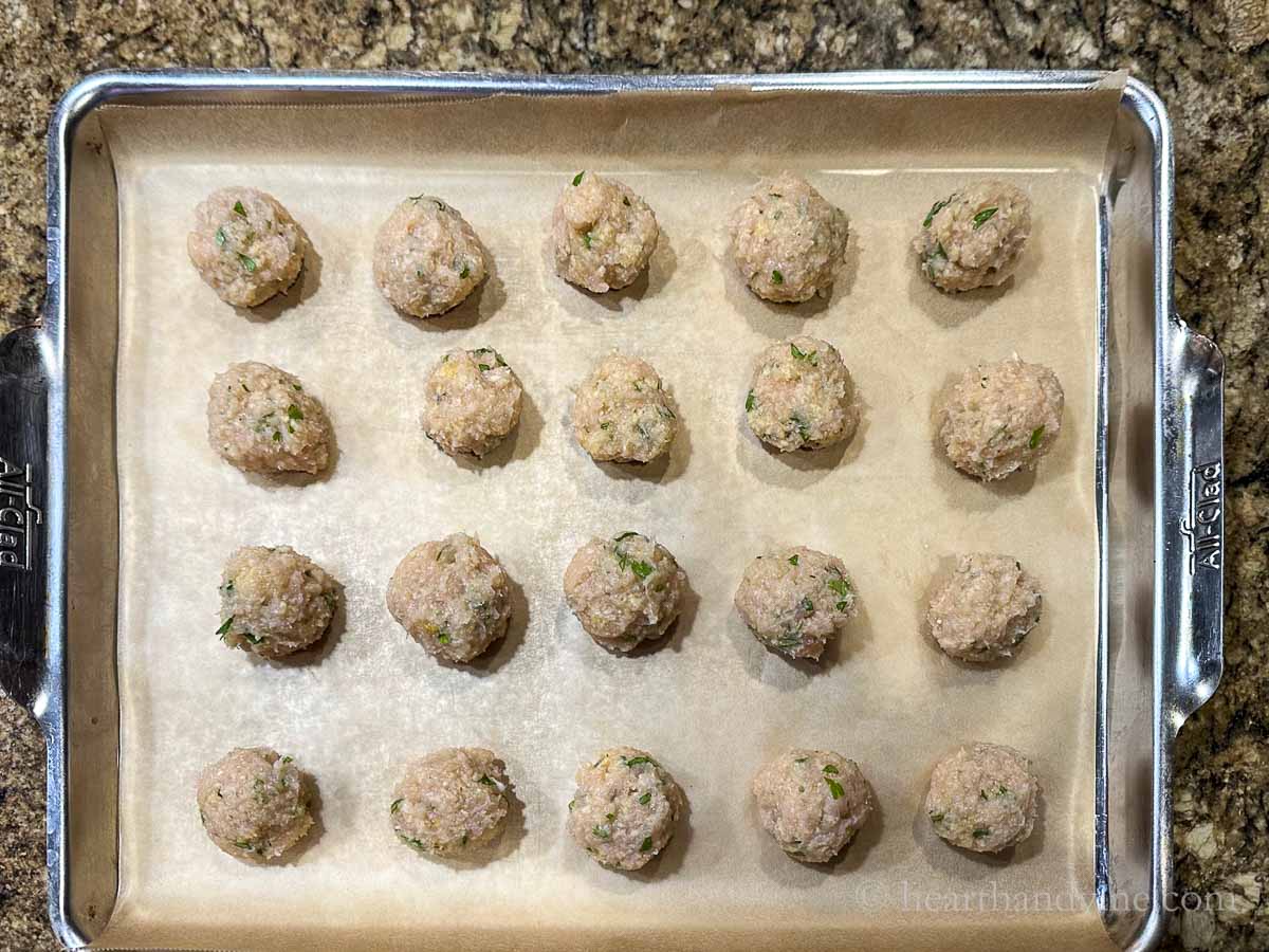 Raw chicken meatballs on a baking pan.