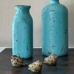 Two painted bottles on a table with three little birds in front.