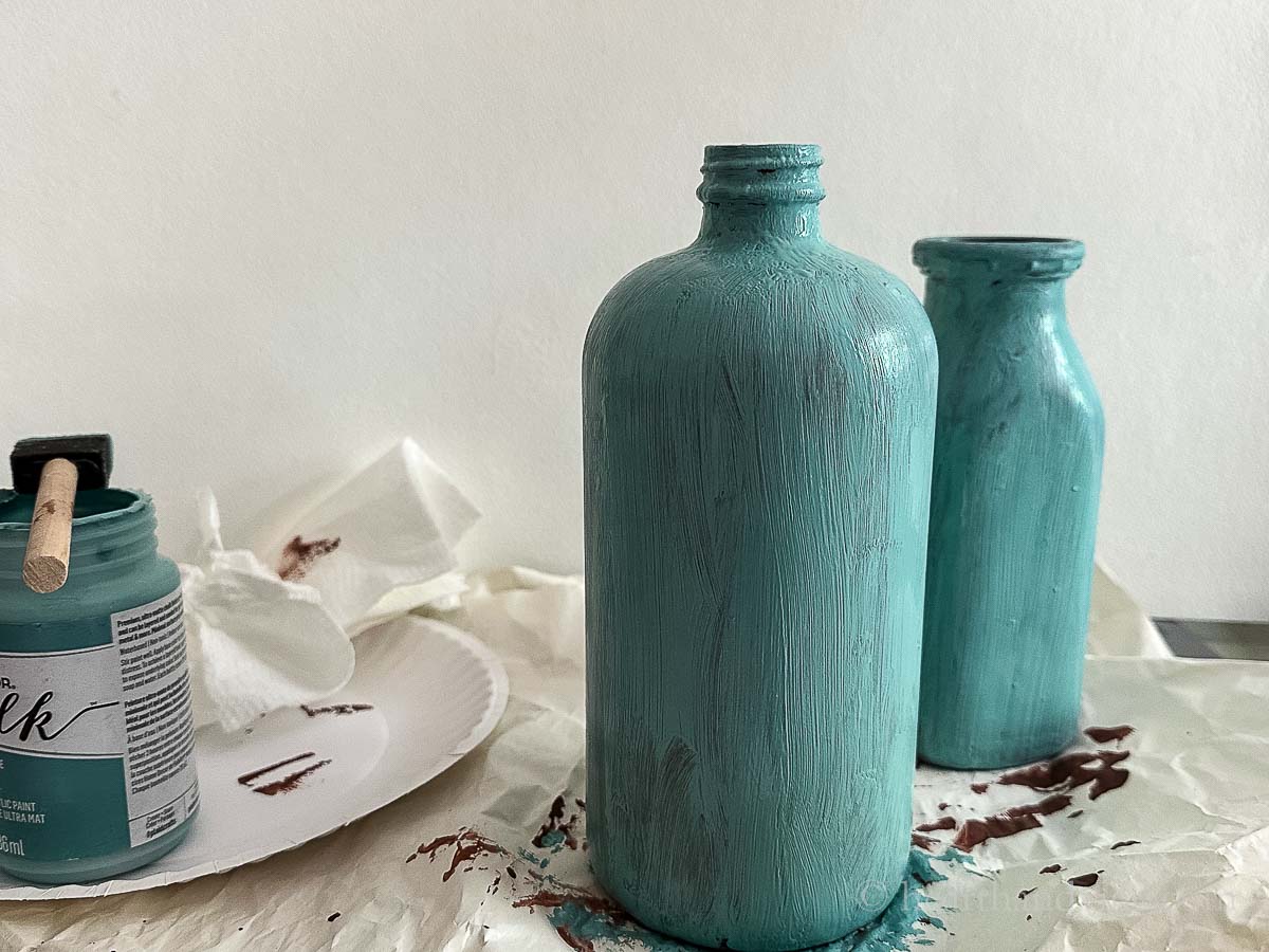 One coat of blue paint on top of the brown paint of two bottles.