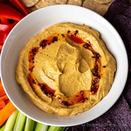 Butternut squash dip in a white bowl with chili pepper oil drizzle around the edge.