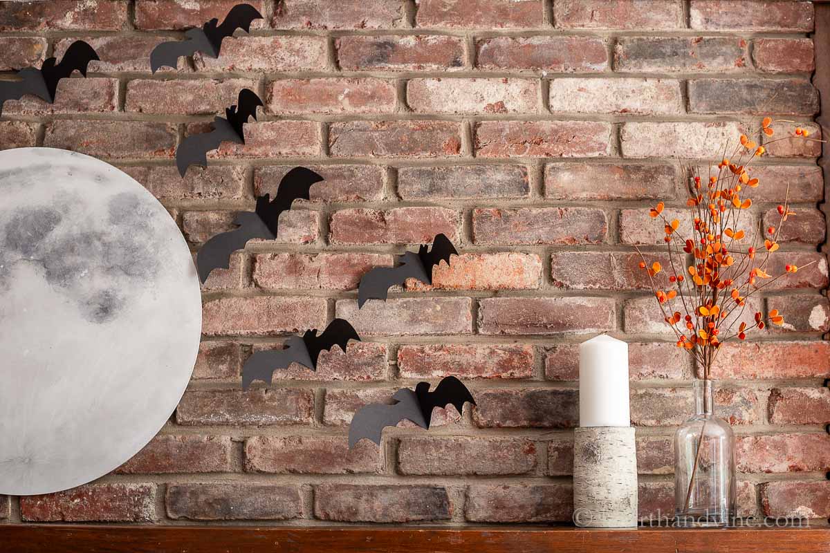 Side of the mantel showing a candle, some orange berries in a bottle vase, a partial view of the full moon and some of the flying bats.